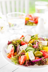 Greek salad. Fresh vegetable salad with tomato, onion, cucumber, pepper, olives, lettuce and feta cheese. Greek salad on plate on white table