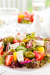 Greek salad. Fresh vegetable salad with tomato, onion, cucumber, pepper, olives, lettuce and feta cheese. Greek salad on plate on white table