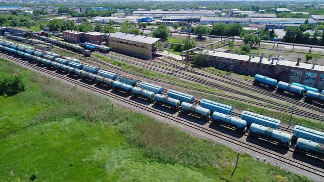 Aerial view of a large train of tanks on the rails next to the production buildings. The camera flies over a long train of tanks standing on the rails.