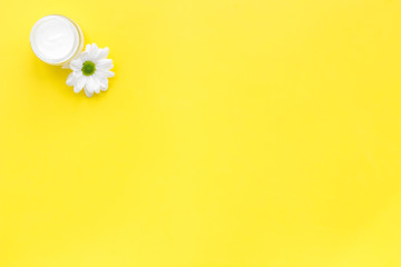 Moisturizing cream based of natural herbal ingredients. Chamomile cream in small jar near chamomile flowers on yellow background top view copy space