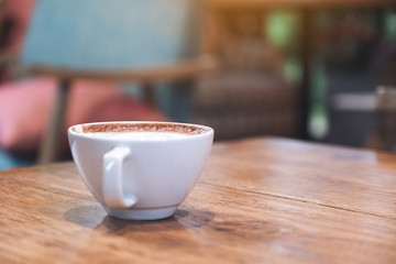 Closeup image of a white cup of latte coffee on wooden table in cafe with blur background