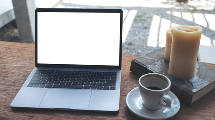 Fototapeta premium Mockup image of laptop with blank white desktop screen and coffee cup , book , candle on wooden table in modern cafe