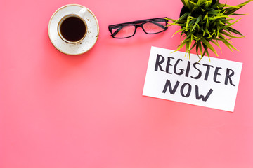 Membership concept. Template for registration. Register now hand lettering iconon word desk with glasses, coffee, plant on pink background top view space for text