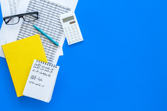 Math homework. Math textbook or tutorial near sheet with numbers, countes, calculator, notebook with formula on blue background top view copy space