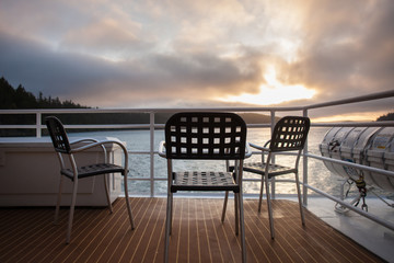 Fototapeta na wymiar Outdoor chairs on the deck of a cruise ship with sunset behind