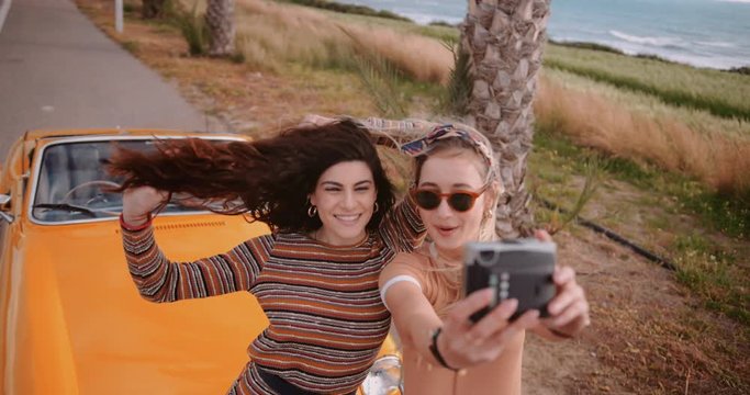 Women on island road trip taking selfies with polaroid camera