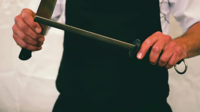 Slow-motion medium shot of a chef sharping a kitchen knife