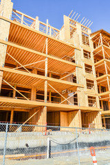 Six storey frame building under construction bordered with metal fence. Woodframe building on concrete base