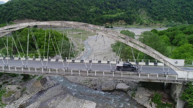 Aerial view. Black pickup truck are moving through old concrete bridge over the mountain river. The camera flies near the bridge.