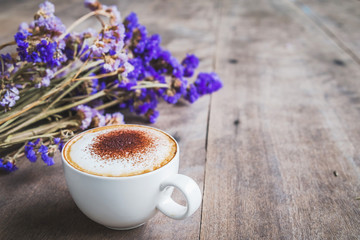 A cup of coffee with bouquet of violet dried flowers on wooden floor background.