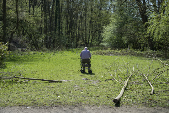 Senior auf Rolator sitzend auf Wiese im Park