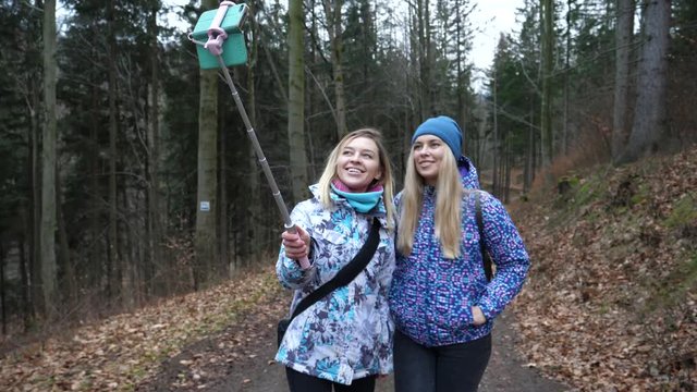 Cute blonde ladies girls friend hang out walking in forest enjoy taking selfie stick pictures
