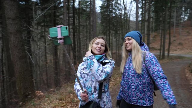 Cute blonde ladies girls friend hang out walking in forest taking selfie stick pictures