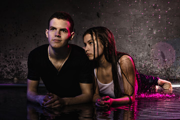 Couple young Teens together in small pool, drops of water and colored light