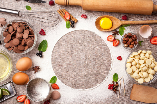 Concept of cooking pies, cakes, pastries and biscuits. Confectionery stock lies on a table, corolla, eggs, white, milk, black chocolate, flour and berries, strawberries, mint, with text space