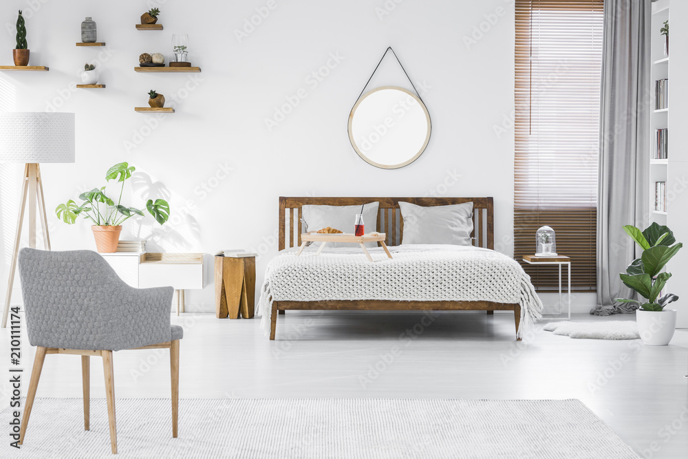 Wall mural Gray, modern armchair, breakfast tray on a double bed and wooden furniture in a simple, stylish apartment room interior with white walls