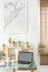 Laptop with an empty screen where you can place your photo, map on the wall and wooden shelves with cactus