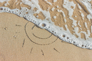 Waves with foam blue  sea on a sunny sandy beach in resort on summer vacation rest. Symbol of the sun drawing on the sand.