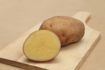Raw potato vegetables potato or russet potato, whole and half on wooden chopping block.