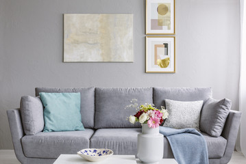 Modern painting and two gold posters hanging on the wall in grey sitting room interior with sofa with pillows and fresh colorful flowers in ceramic vase - obrazy, fototapety, plakaty