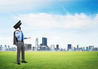 Camera headed man standing on green grass against modern cityscape