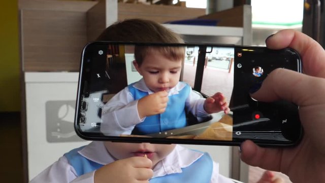 Mother takes pictures via mobile phone of her child boy eating fast food for social media