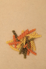 Raw three color spiral twist pasta scattered on brown plywood backgrounds with space for text.