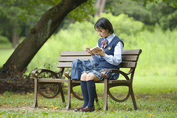 ベンチに座って本を読む女子校生