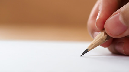Closeup student hand holding pencil writing on paper with blurred background, business and...