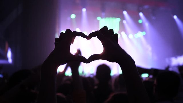 Making heart silhouette girl fingers sway hand enjoy music concert in a spectators crowd