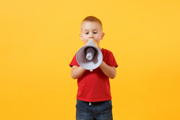 Little cute kid baby boy 3-4 years old in red t-shirt holding in hand, speaking in electronic gray megaphone, looking camera isolated on yellow background. Kids childhood lifestyle concept. Copy space