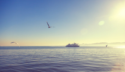 Silhouette of a ferry boat at sunset and seagulls fly around. Beautiful atmospheric bright landscape, Lisbon, Portugal