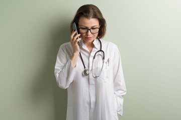 Positive doctor woman talking mobile phone. Background green wall in the clinic