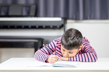 Naklejka premium Young Asian boy tired write on the note book by pencil in the room