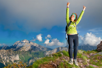 Girl in the summit at the mountain raises her arms happy