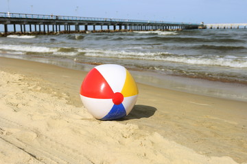 Obraz premium Colorful beach ball on sand and waving sea. Holiday beach ball near Baltic sea and Palanga bridge in horizon.