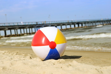 Colorful beach ball on sand and waving sea. Holiday beach ball near Baltic sea and Palanga bridge in horizon.