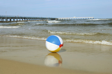 Colorful beach ball on sand and waving sea. Holiday beach ball near Baltic sea and Palanga bridge in horizon.