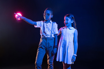 Fototapeta premium Amazement. Cheerful afro-american boy pressing imaginary buttons and a surprised girl standing near him