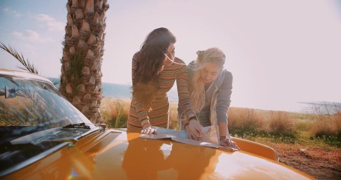 Young hipster women reading map on convertible car road trip