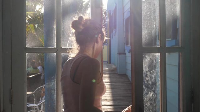 Woman goes away shutting the transparent glass door of wooden house in sun rays