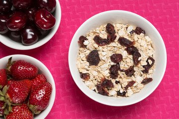 on a pink mat for fitness three plates, in muesli, strawberry and cherry, the concept of sport and healthy eating, close-up