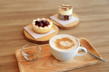 Confectioners atmosphere concept. Cup of hot latte coffee on wooden table with some of cake dessert at background.