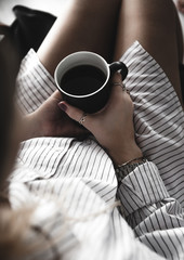 Female hands holding a white cup of tea, burgundy manicure, the girl is dressed in a shirt