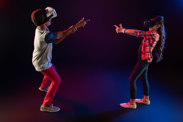 Fototapeta premium Shooting. Alert sweet girl and a boy wearing VR headsets and playing an interesting game