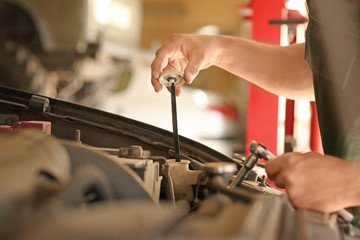 Young mechanic checking engine oil level in car service center