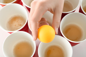 Woman holding yellow ball over cups arranged for playing beer pong, closeup