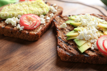 Tasty toasts with avocado on wooden board