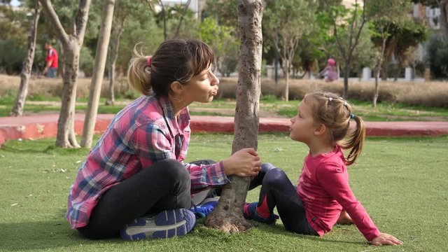 Familyt fun, kid girl daughter with young mother playfully kiss together in park