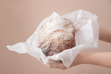Woman holding fresh tasty bread on color background, closeup